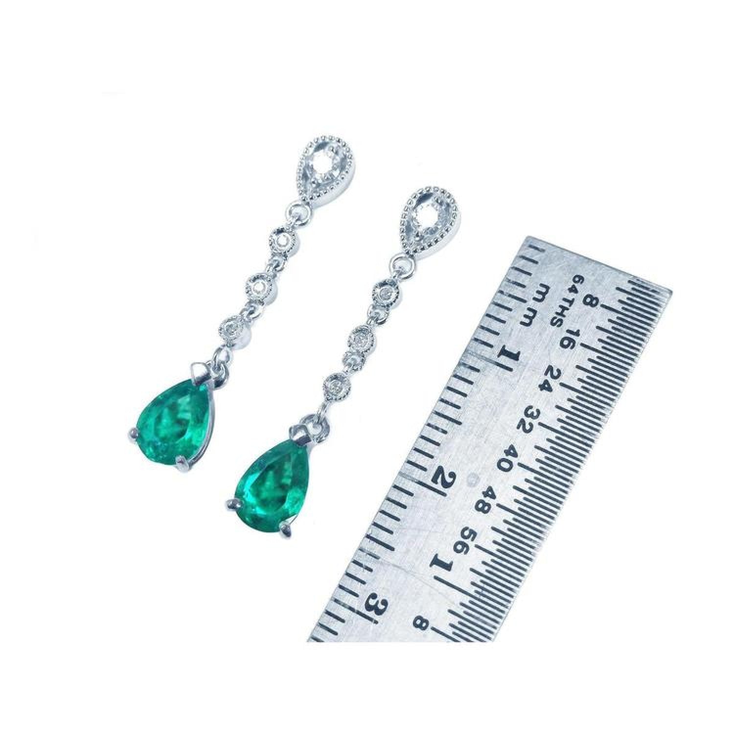1.05 ct. pear-shaped emerald drop earrings in 14K white gold with diamonds, next to a ruler.