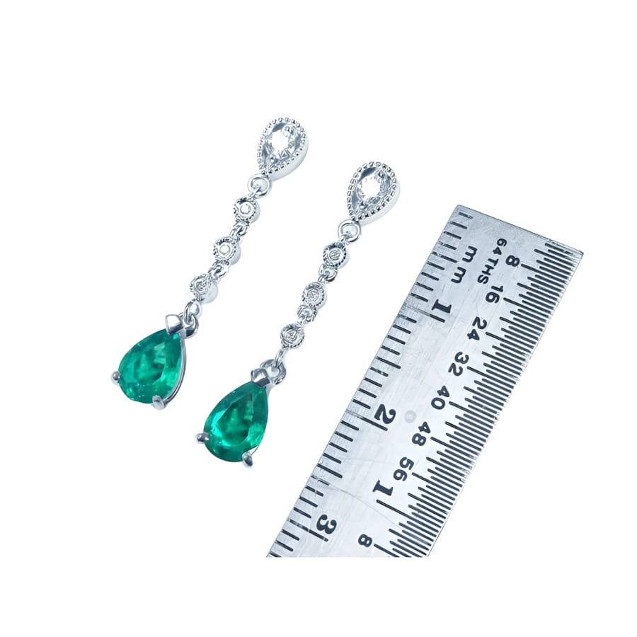 1.05 ct. pear-shaped emerald drop earrings in 14K white gold with diamonds, next to a ruler.