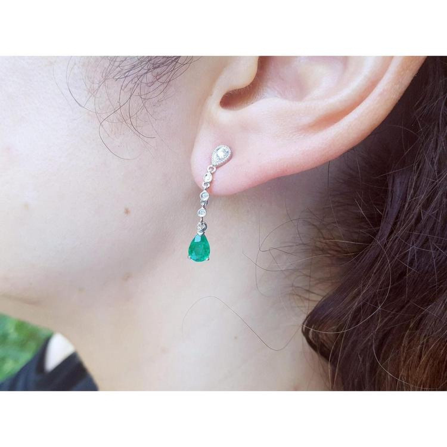 14K white gold pear-shaped emerald drop earrings with brilliant white diamonds on an ear.