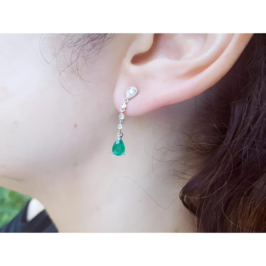 14K white gold pear-shaped emerald drop earrings with brilliant white diamonds on an ear.