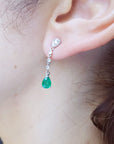 Close-up of a woman wearing emerald teardrop earring with a blurred background.