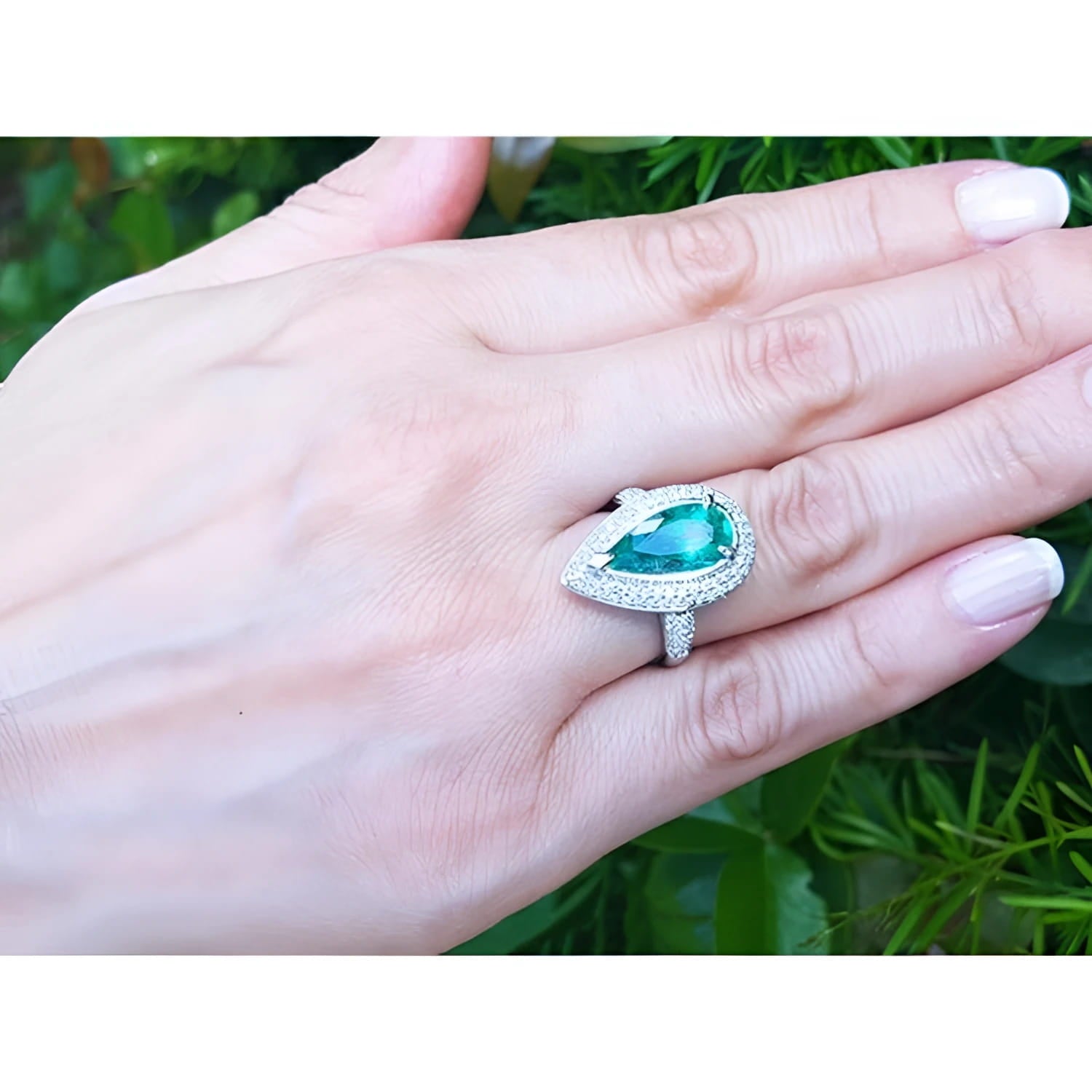 Pear-shaped 3.35 ct. emerald engagement ring in 14K white gold with diamond halo on a hand.