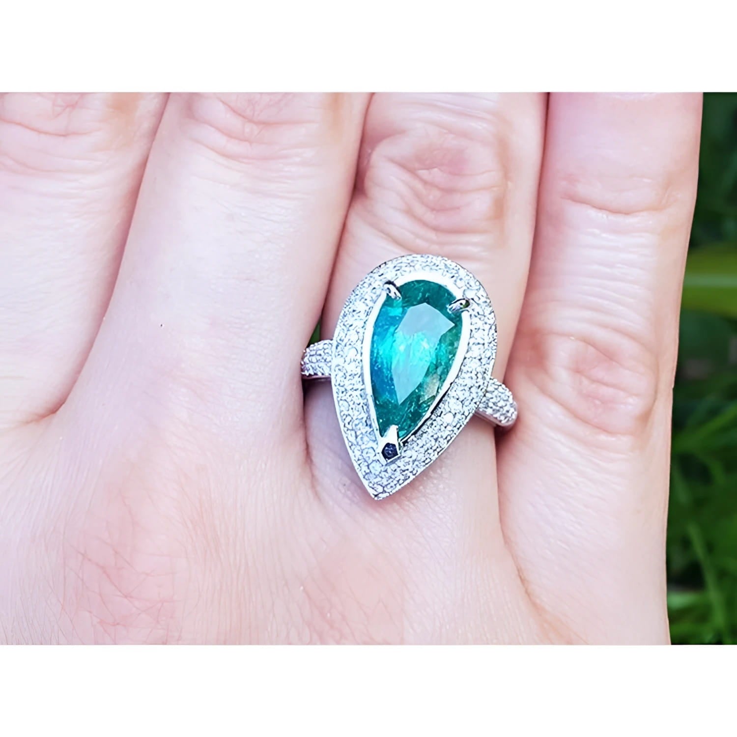 Ladies' ring with a pear-shaped natural colombian emerald in a halo diamond on a person's finger.