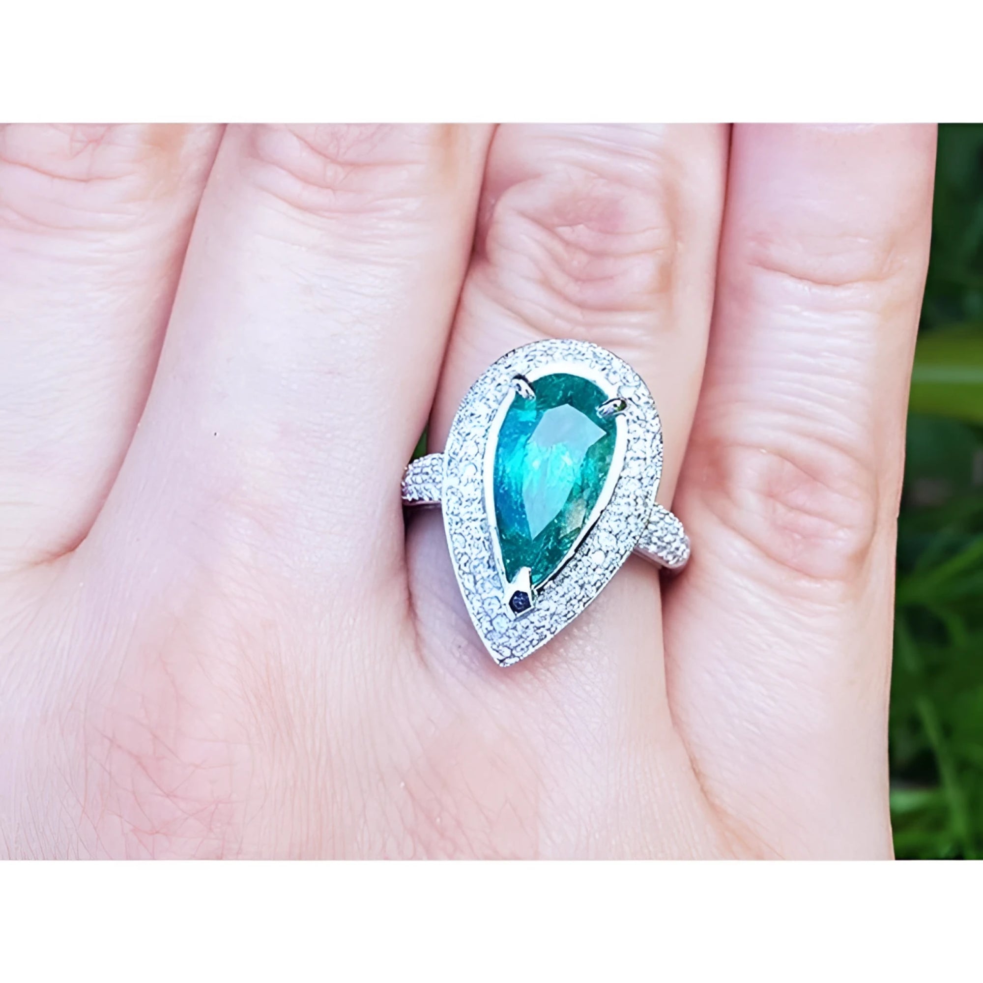 Ladies' ring with a pear-shaped natural colombian emerald in a halo diamond on a person's finger.