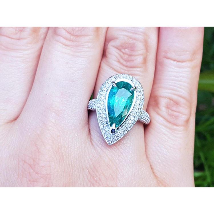 Ladies' ring with a pear-shaped natural colombian emerald in a halo diamond on a person's finger.