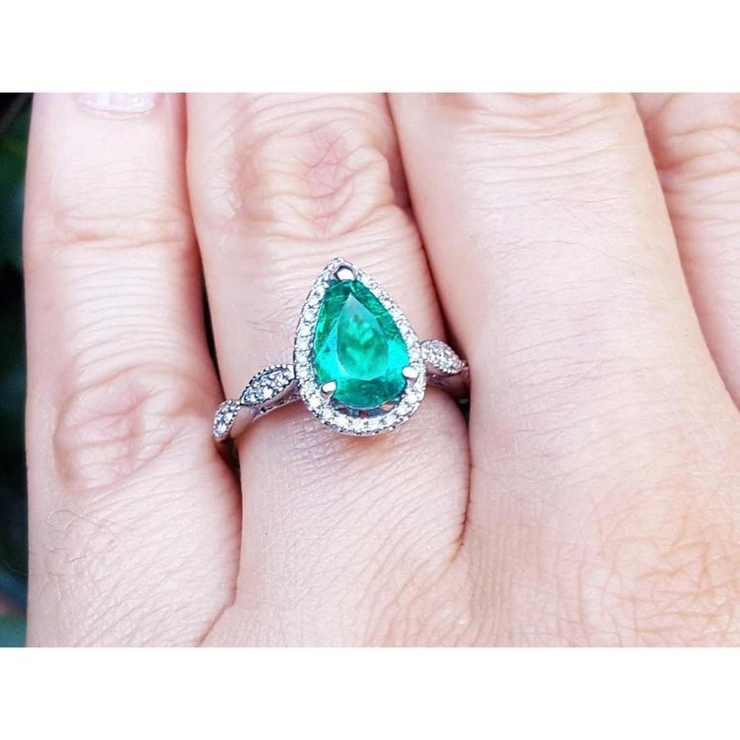 1.43 ct teardrop emerald engagement ring in 14K white gold with diamond halo and twisted band on a hand.