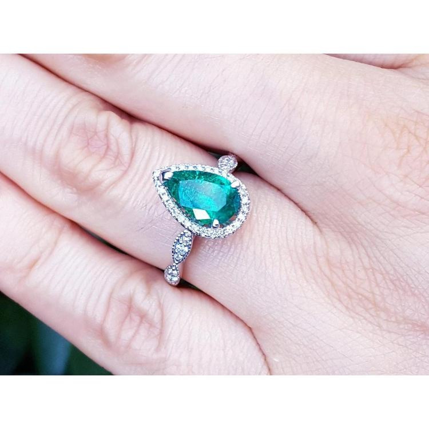1.43 ct teardrop emerald engagement ring in 14K white gold with diamond halo and accents on a hand.