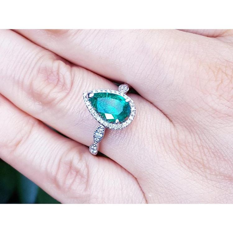 1.43 ct teardrop emerald engagement ring in 14K white gold with diamond halo and accents on a hand.