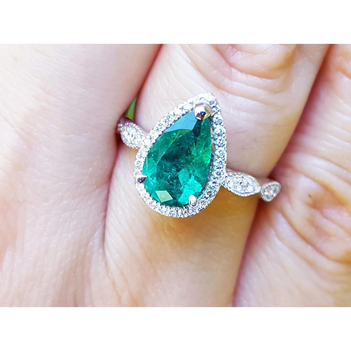 Pear cut emerald ring with a halo diamond in white gold on a finger.