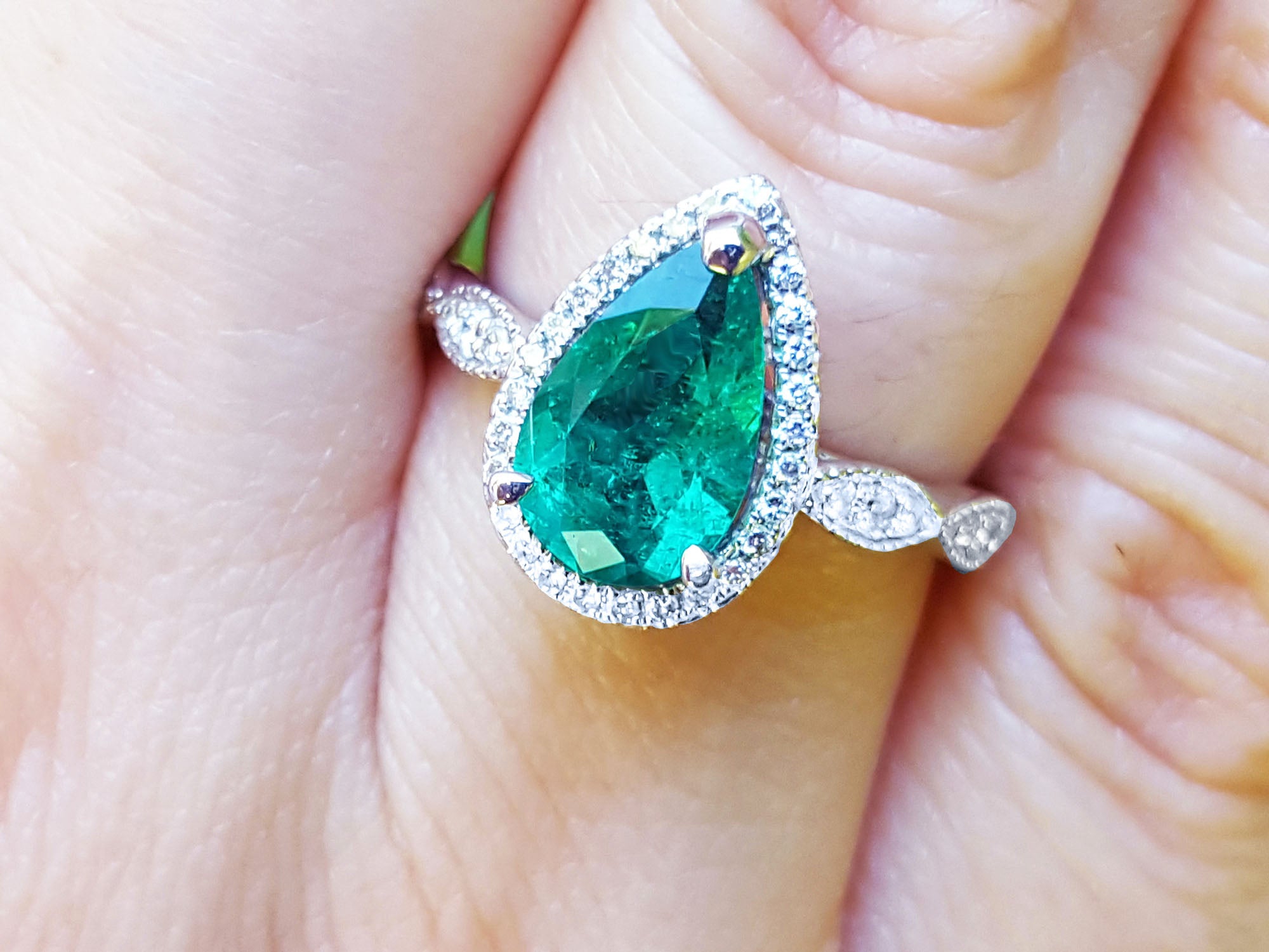 Pear cut emerald ring with a halo diamond in white gold on a finger.