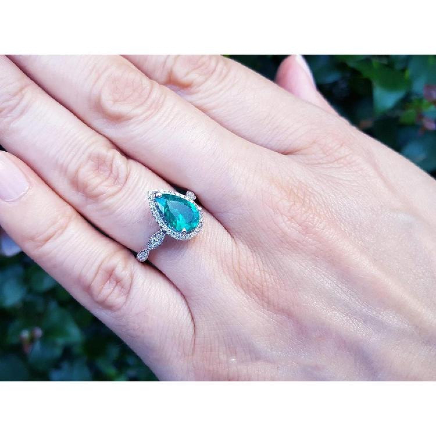 1.43 ct teardrop emerald engagement ring in 14K white gold with diamond halo on a hand.