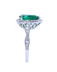 A white gold ring with a teardrop emerald and diamond-studded band on a white background.