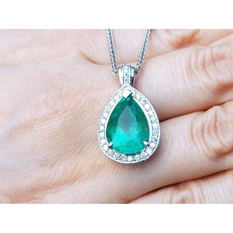 Green teardrop emerald gemstone pendant on a white gold chain held between fingers.