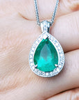 Green teardrop emerald gemstone pendant on a white gold chain held between fingers.