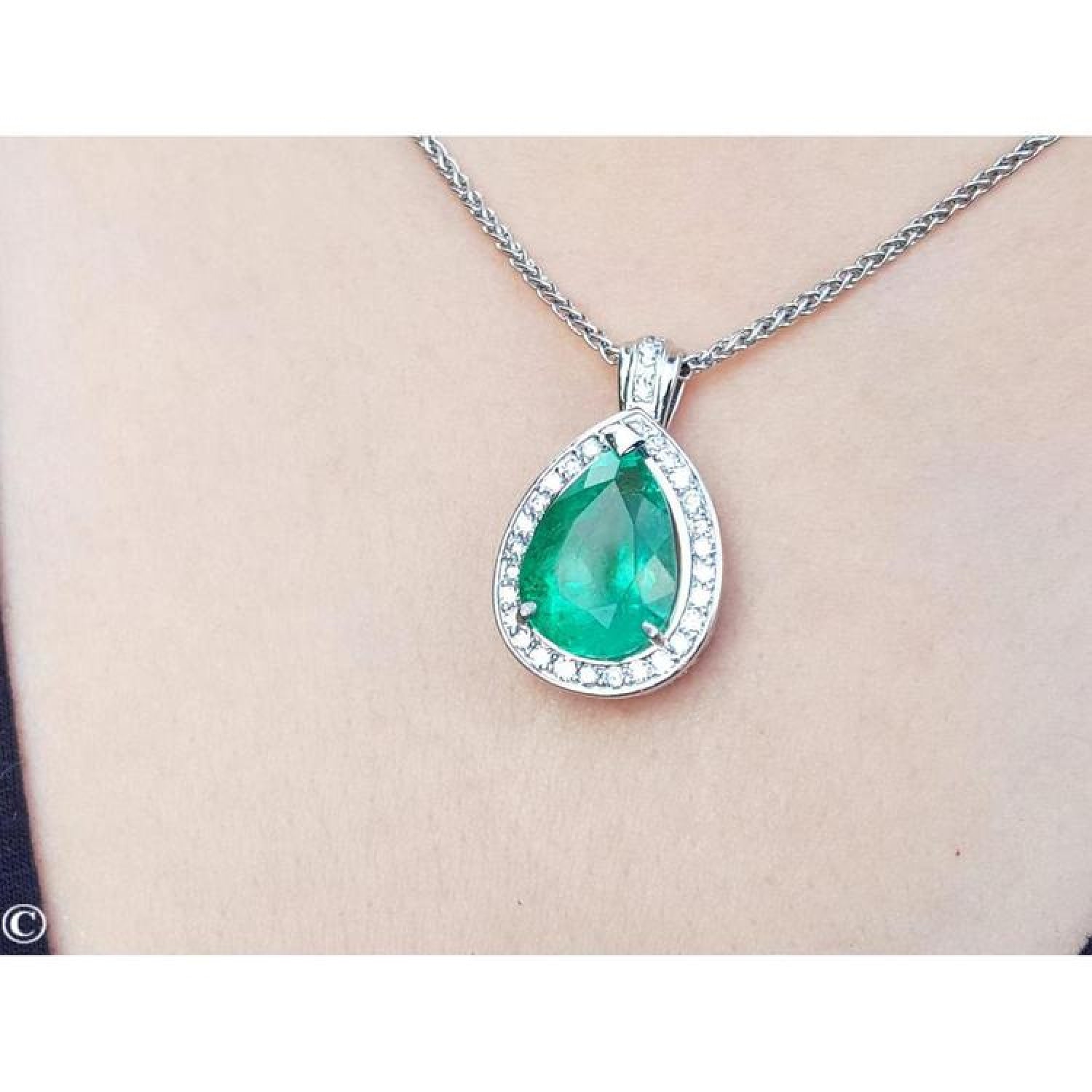 Pear-shaped emerald pendant with halo diamonds in 14K white gold, worn on a chain.