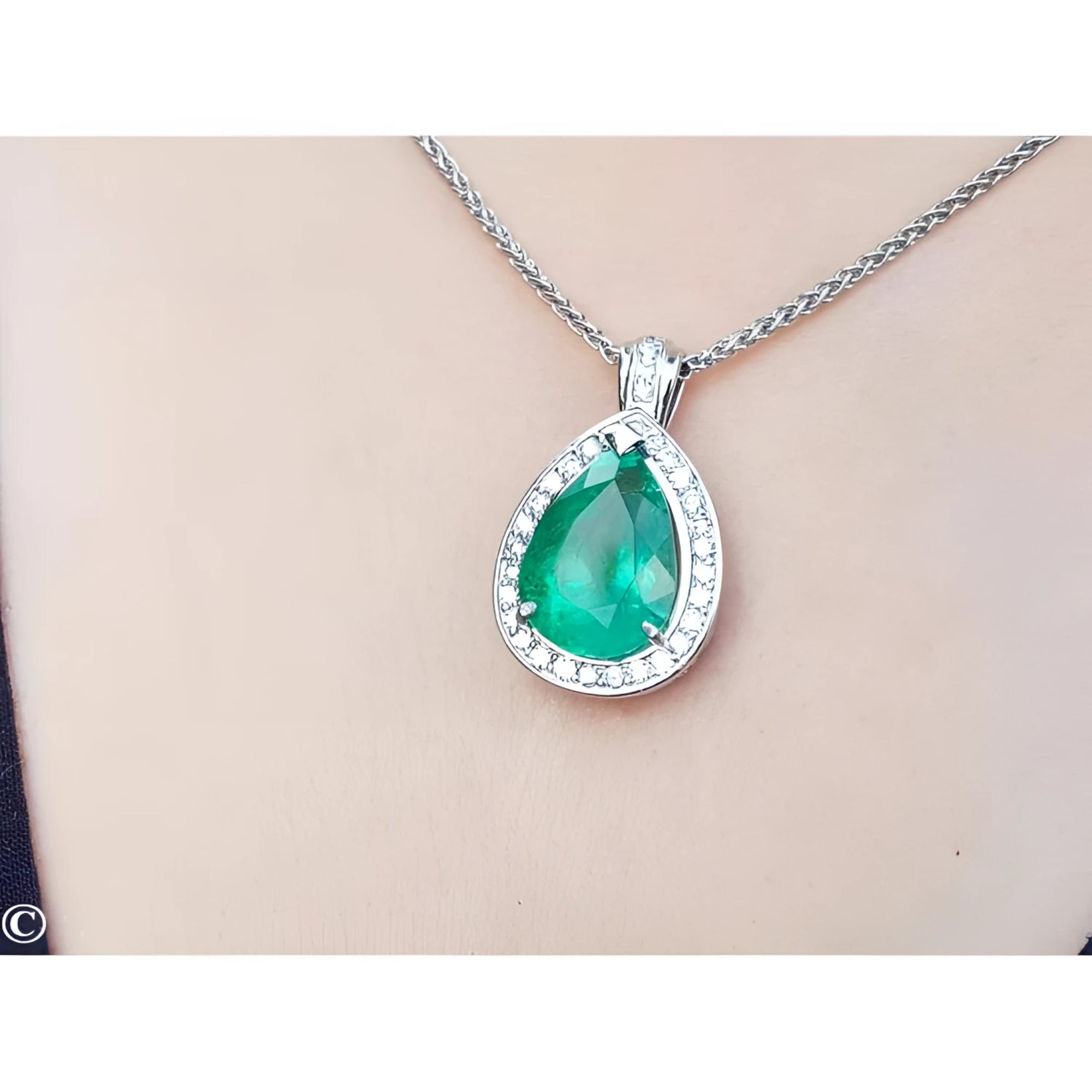 Pear-shaped emerald pendant with halo diamonds in 14K white gold, worn on a chain.
