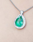 A white gold necklace with a natural emerald teardrop pendant on a beige skin background.