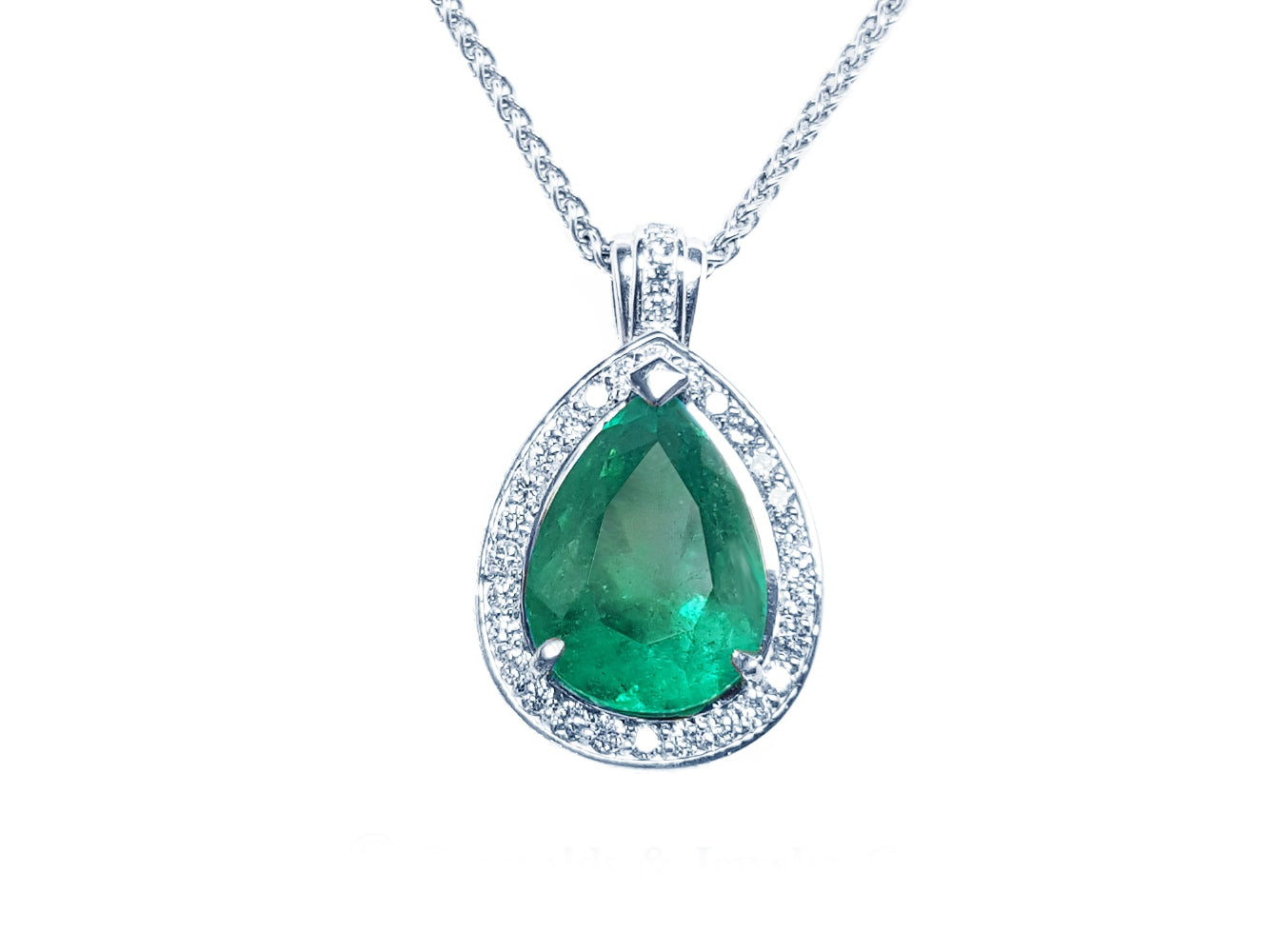 Emerald teardrop pendant with diamond halo on a topside view.