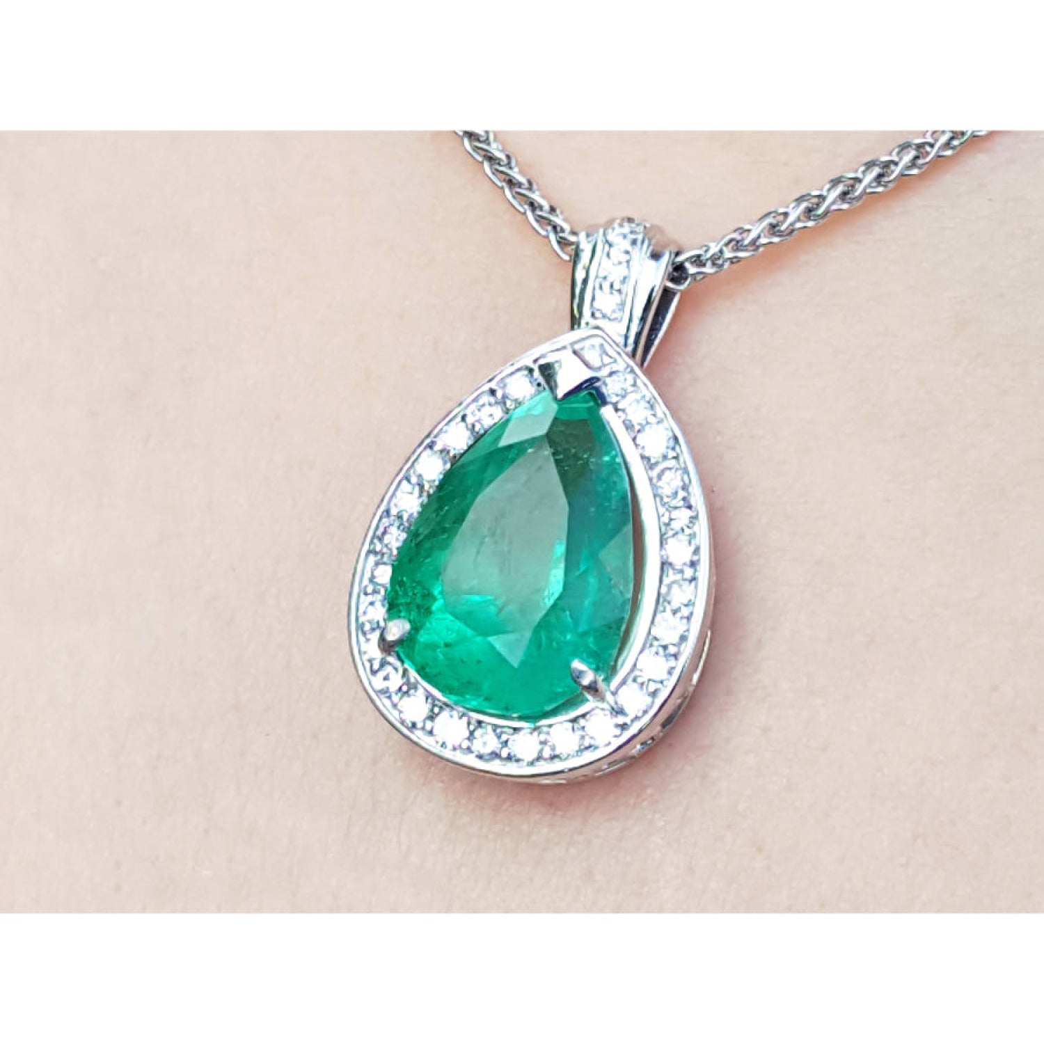 8.64 ct. pear-shaped emerald pendant with diamond halo in 14K white gold, shown on a chain against a light skin-tone background.