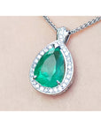 8.64 ct. pear-shaped emerald pendant with diamond halo in 14K white gold, shown on a chain against a light skin-tone background.