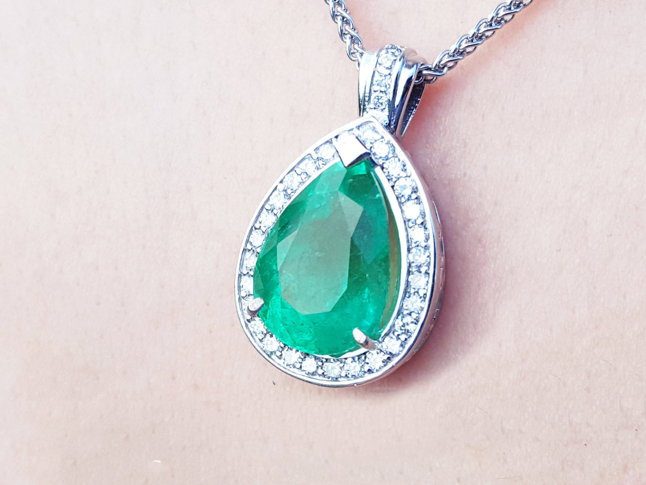 Green teardrop emerald pendant with white gold chain on a person&#39;s neck