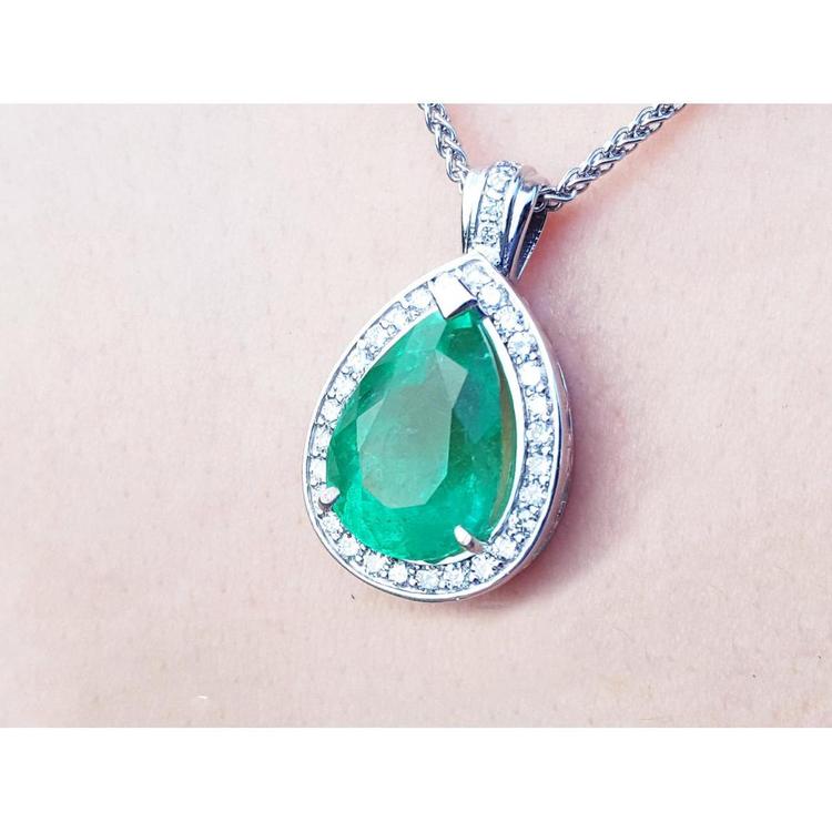 Green teardrop emerald pendant with white gold chain on a person's neck