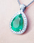 Green teardrop emerald pendant with white gold chain on a person's neck