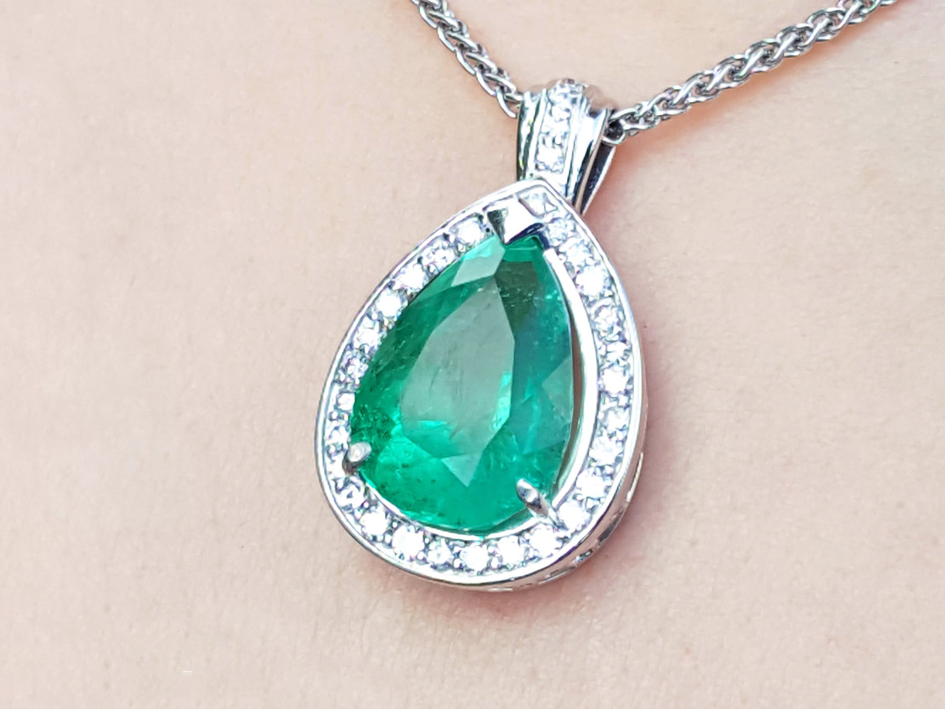 Green emerald pendant with white gold chain on beige skin background