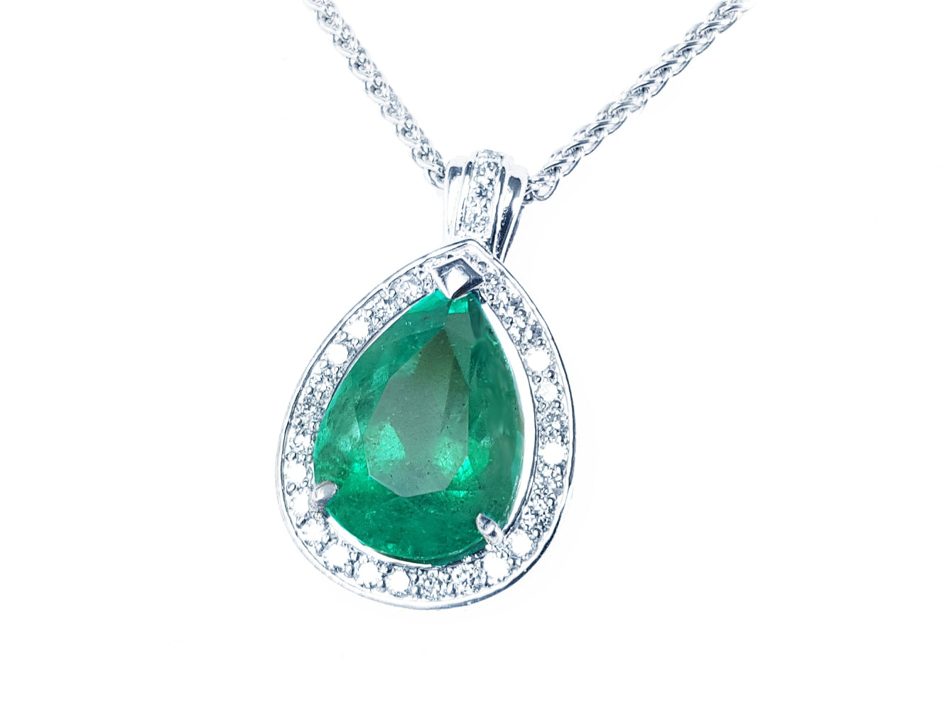 Emerald green teardrop pendant with diamond halo on a left side position topside visible.