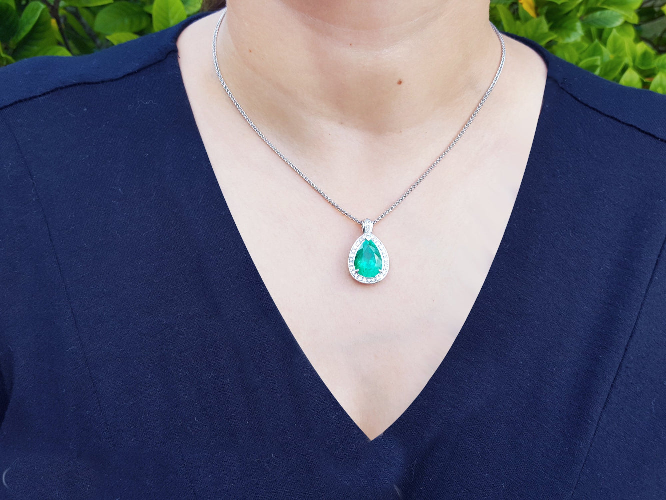 Person wearing a necklace with an emerald pendant against a blurred green background