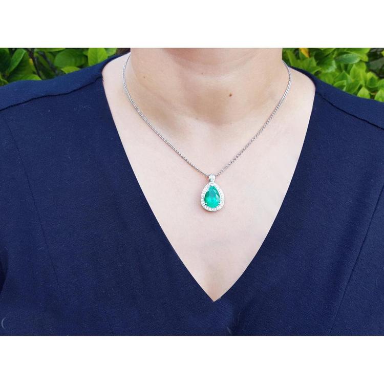 Person wearing a necklace with an emerald pendant against a blurred green background