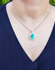 Person wearing a necklace with an emerald pendant against a blurred green background