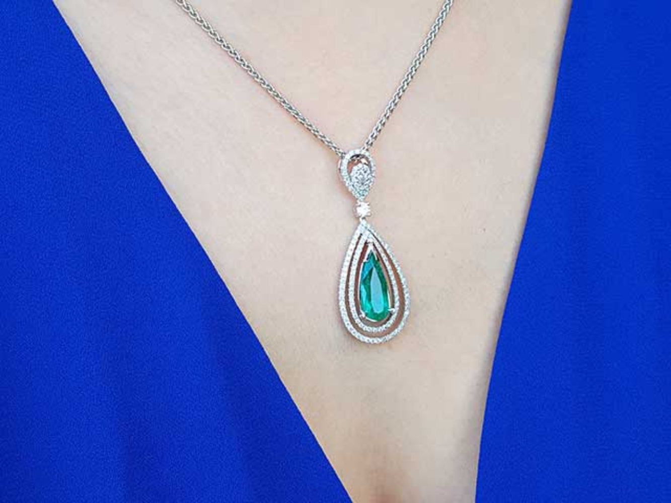 Teardrop-shaped emerald pendant on a white gold chain on a person&#39;s chest