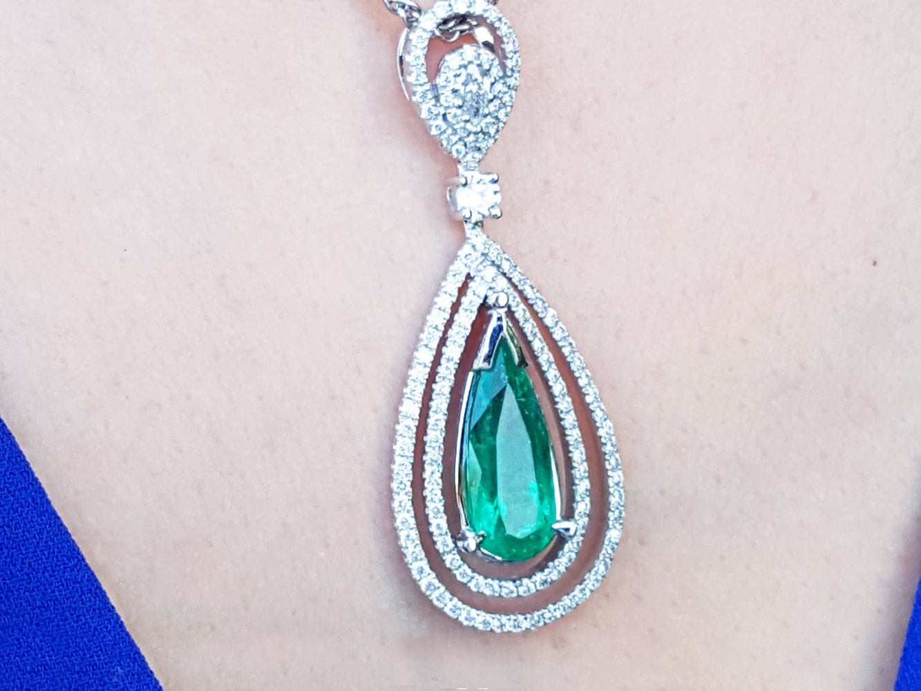 Teardrop-shaped emerald pendant with diamond accents on a person's chest.
