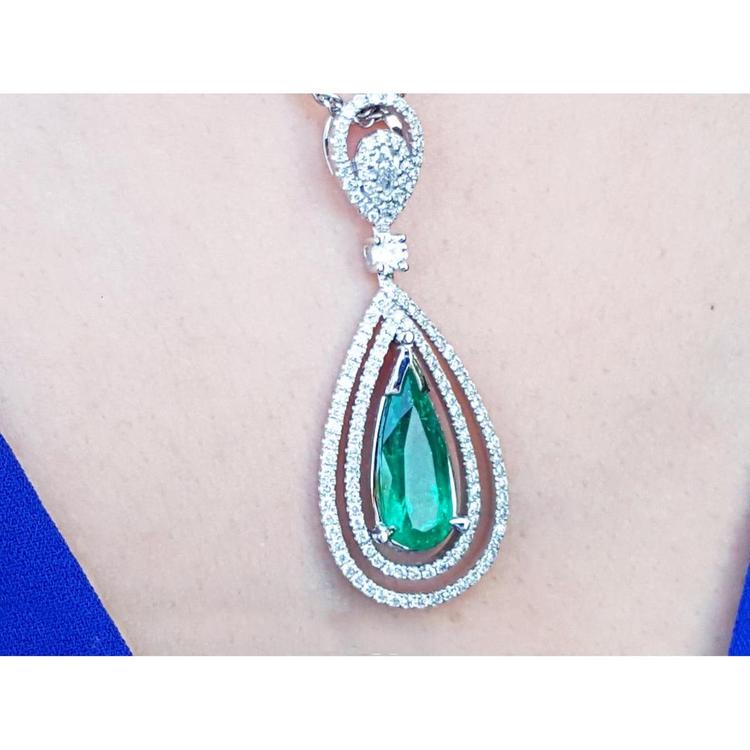 Teardrop-shaped emerald pendant with diamond accents on a person's chest.