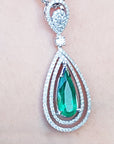 Teardrop-shaped emerald pendant with diamond accents on a person's chest.