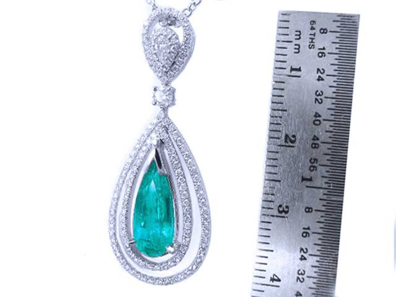 Teardrop-shaped emerald pendant with diamond accents next to a ruler for scale on a white background