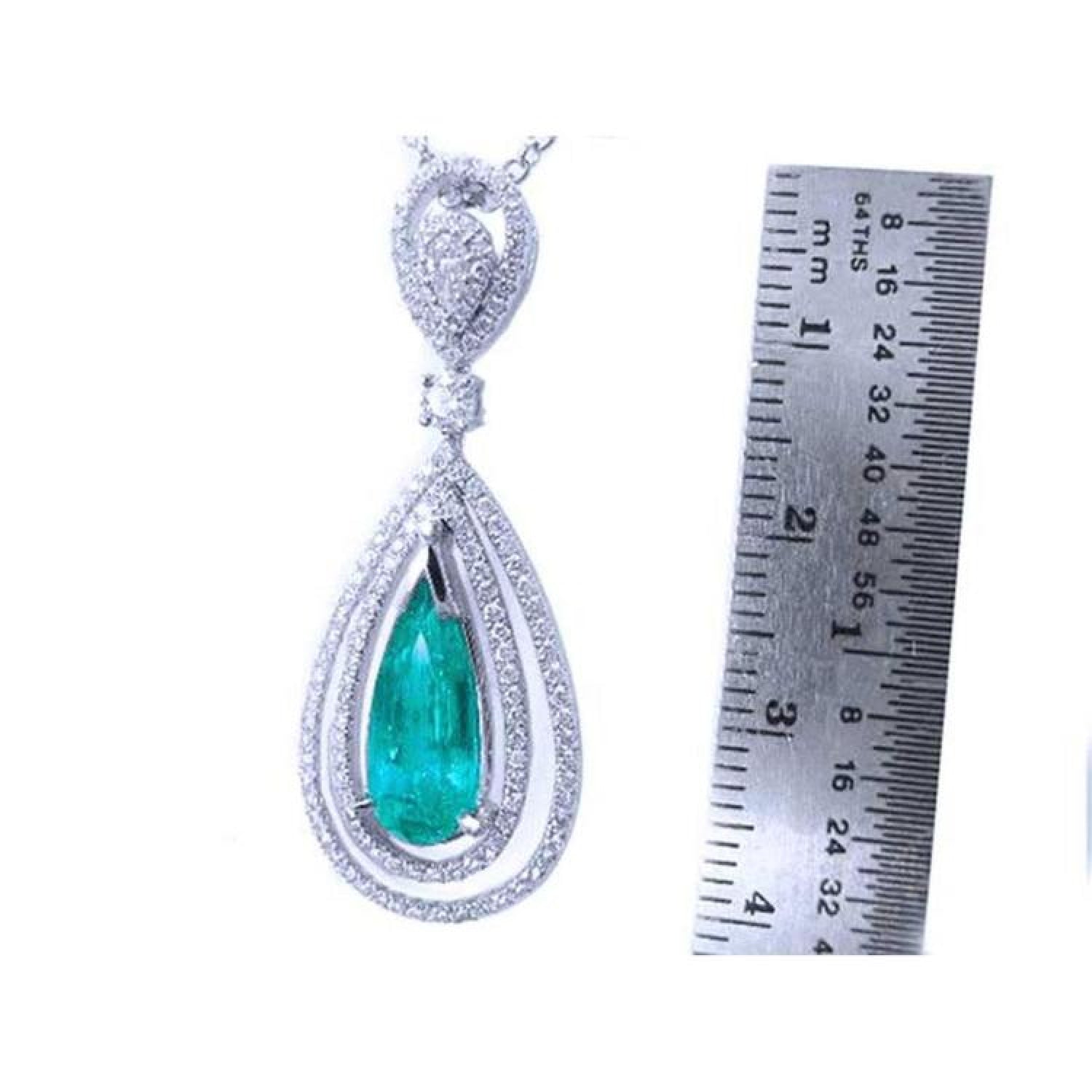 2.13 ct teardrop emerald pendant with double diamond halo in 18K white gold, next to a ruler.