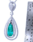 Teardrop-shaped emerald pendant with diamond accents next to a ruler for scale on a white background