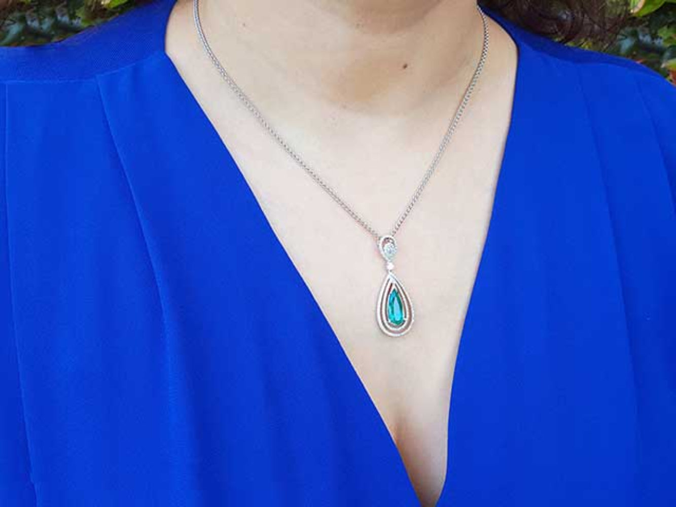 Teardrop-shaped emerald pendant necklace on a person wearing a blue top.