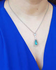 Teardrop-shaped emerald pendant necklace on a person wearing a blue top.
