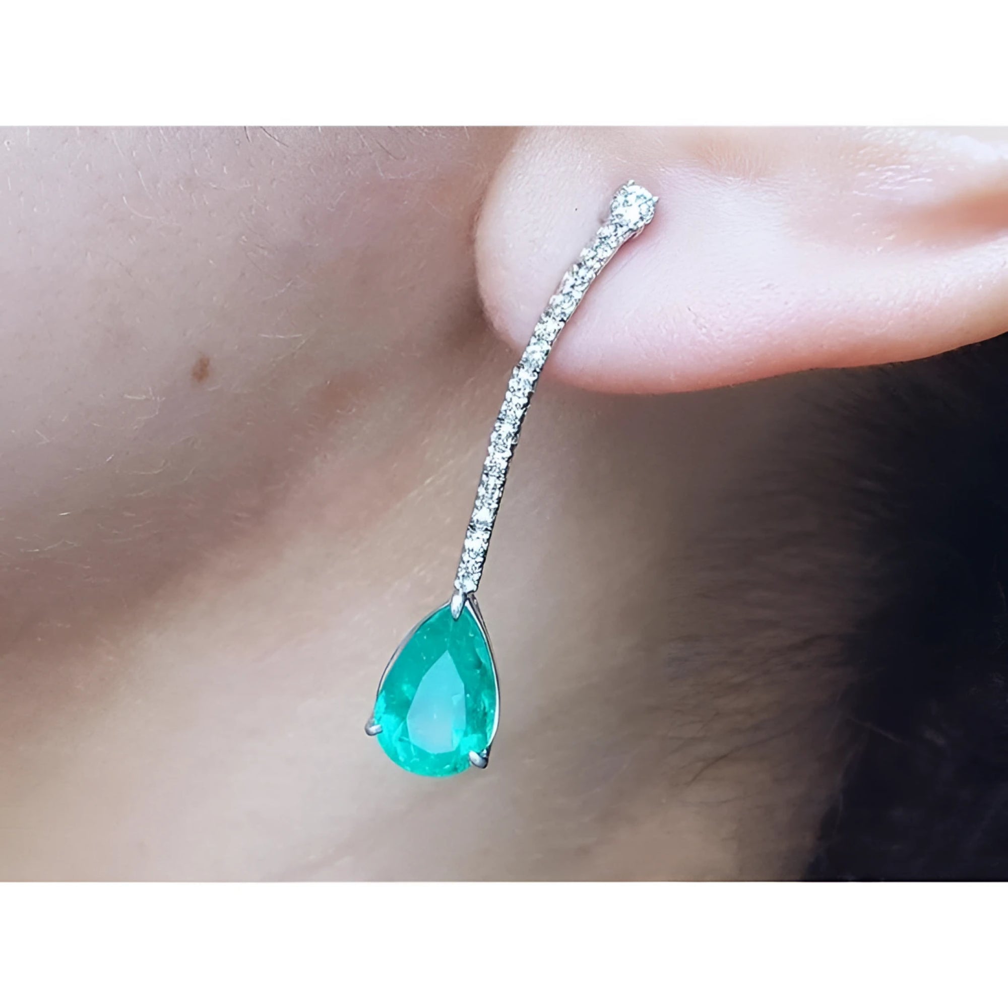 Teardrop emerald green gemstone earring on a person's ear
