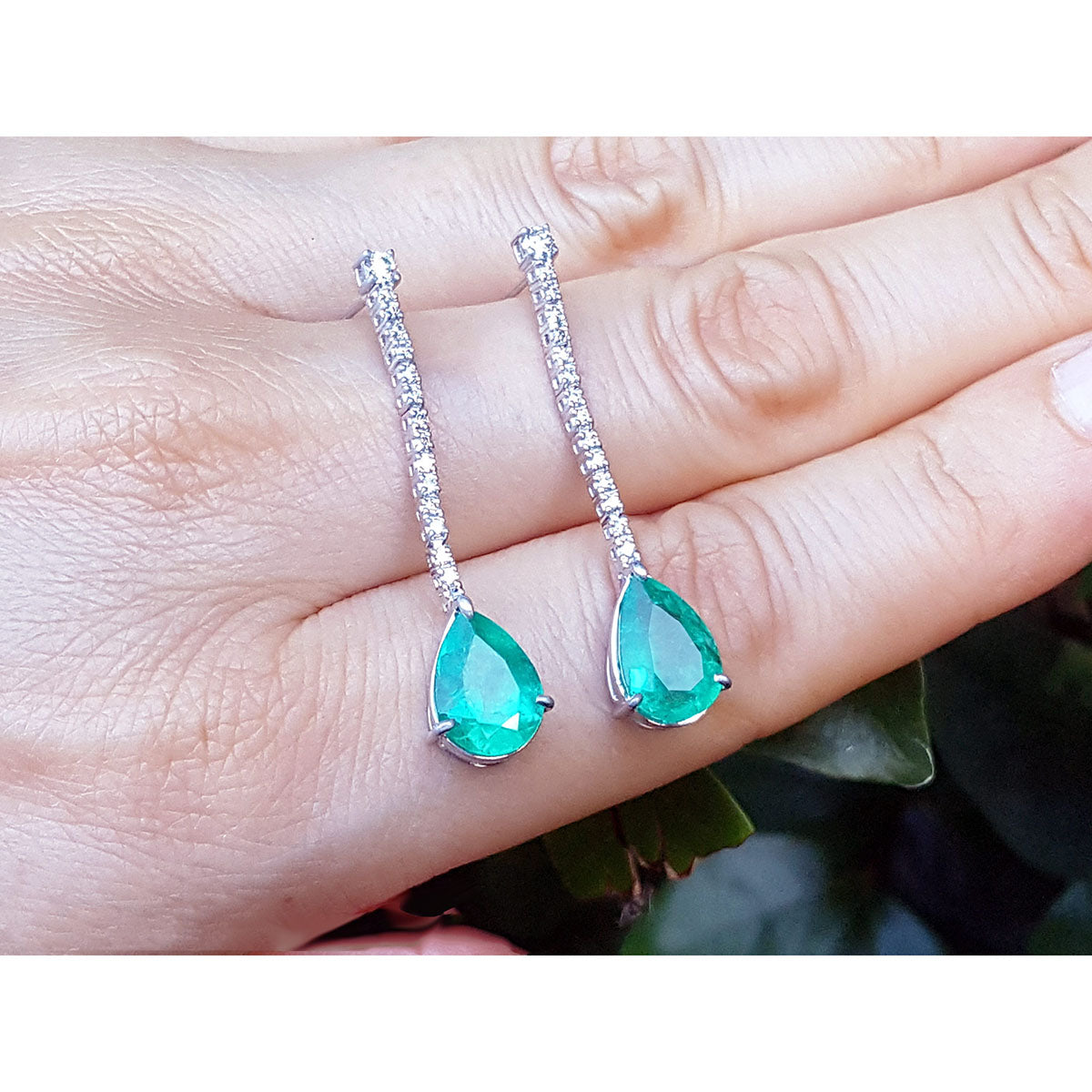 Teardrop-shaped emerald gemstone earrings on a hand with a blurred background