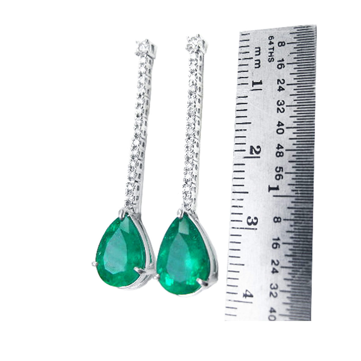 Pair of emerald teardrop earrings with white gold detailing next to a ruler for scale on a white background