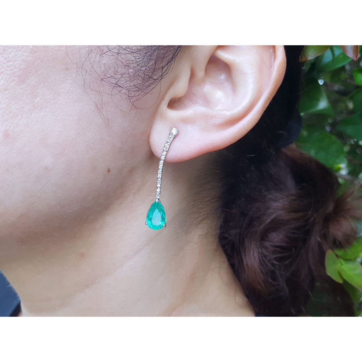 Close-up of an ear wearing a emerald teardrop earring with a blurred background