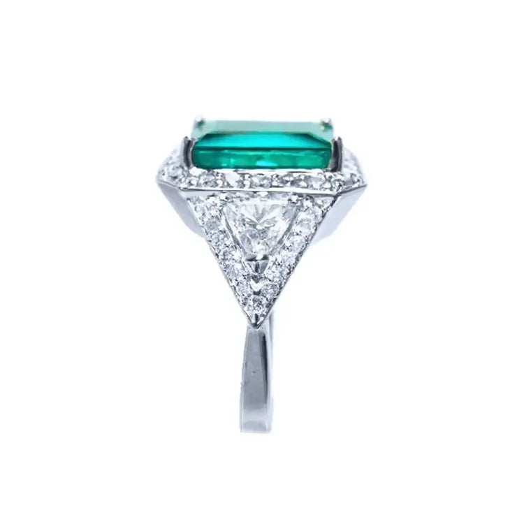 Este anillo en oro blanco para mujer muestra en su parte alta una esmeralda y diamantes redondos y triangulares.