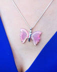 Pink butterfly agate pendant necklace on a person's neck against a blue background