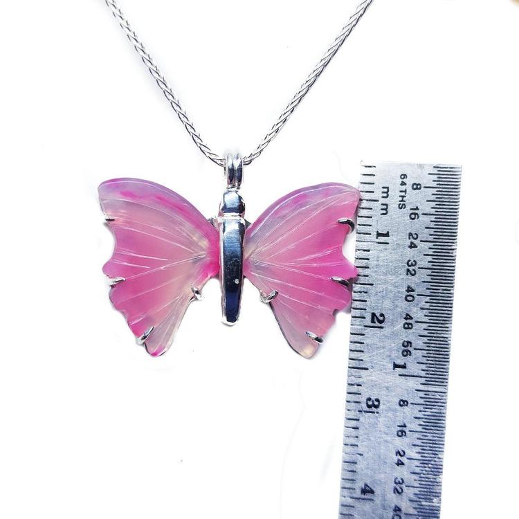 Pink natural agate butterfly pendant with silver setting on a silver chain, next to a ruler.