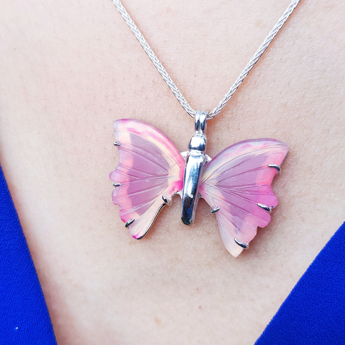 Pink butterfly agate pendant sterling silver necklace on a person&#39;s neck with a blue background