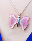 Pink butterfly agate pendant sterling silver necklace on a person's neck with a blue background
